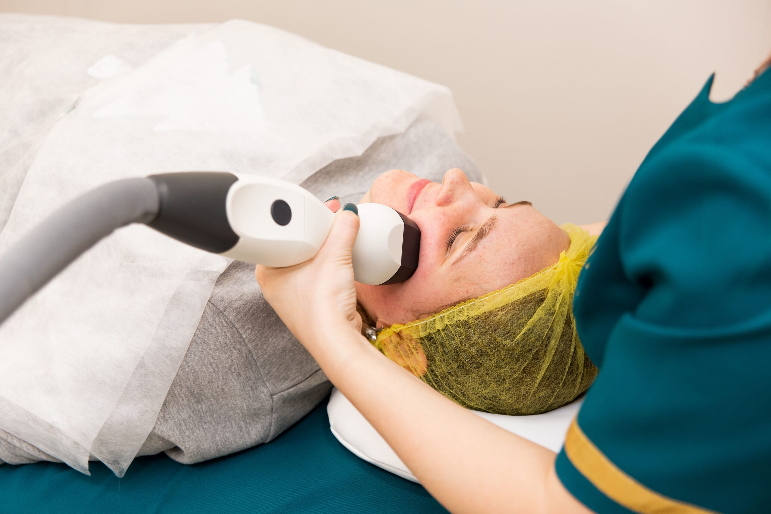 woman laying down receiving laser hair removal wearing a yellow hairnet